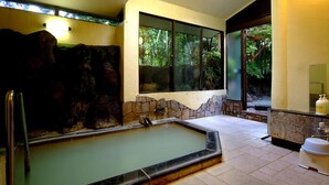 A spa area with a hot tub, stone walls, and a view of greenery through large windows.