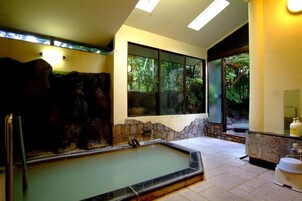 Zona de spa con hidromasaje, paredes de piedra y vistas a la vegetación a través de amplios ventanales.