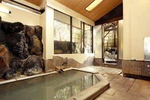A spa area with a stone wall, a hot tub, and a wooden ceiling. - Onsen Ryokan Mitake (Hakone)