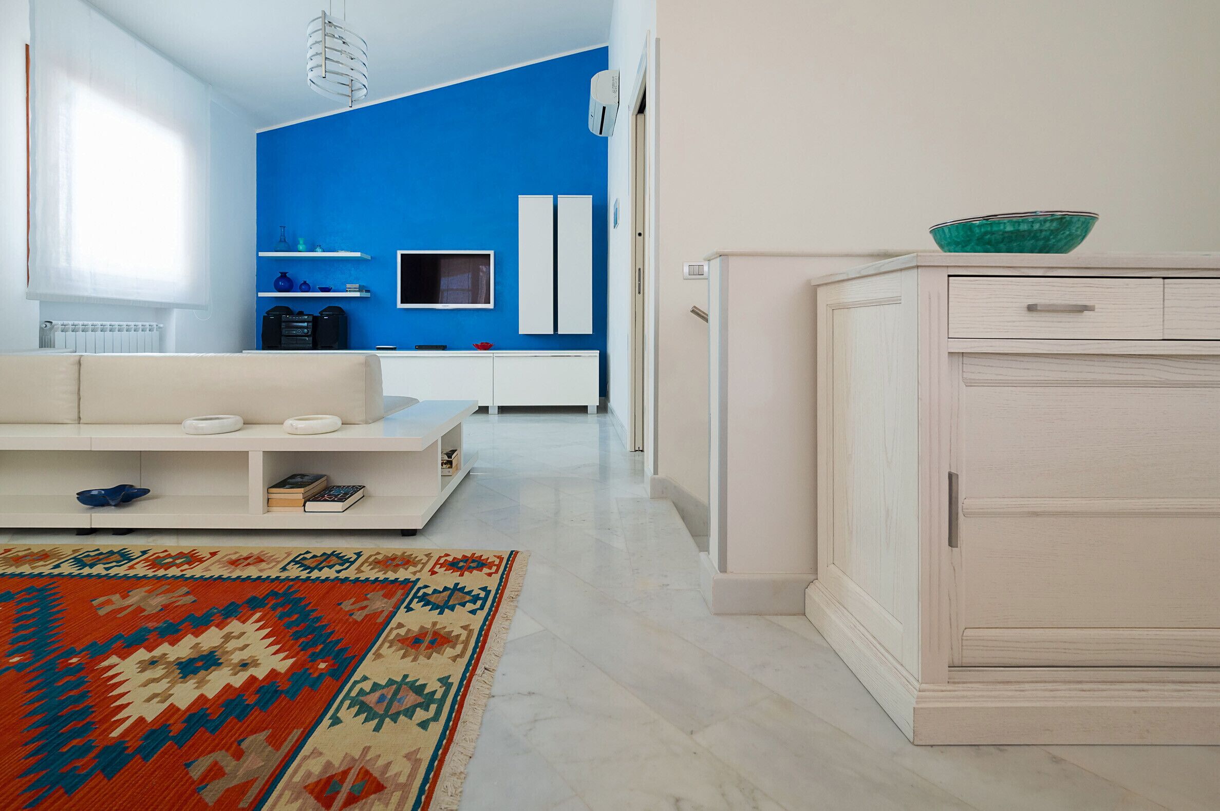 A modern living room with a white sofa, a patterned rug, a blue accent wall, and a white cabinet.