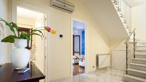 Un pasillo con piso de mármol, un jarrón blanco con una planta, un control remoto y una escalera con barandilla de metal.
