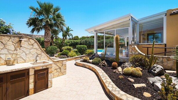 Cocina exterior moderna con pared de piedra, una palmera y un jardín de cactus.