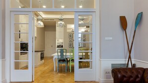 An open door leading to a dining area with a wooden herringbone floor, a dining table with chairs, and a brown leather sofa.