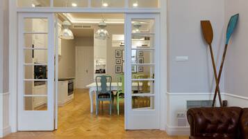An open door leading to a dining area with a wooden herringbone floor, a dining table with chairs, and a brown leather sofa.
