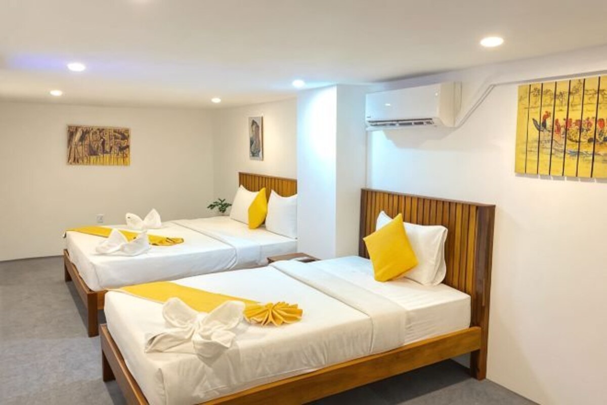 A hotel room with two beds, each with white bedding and yellow accents, wooden headboards, and artwork on the walls.