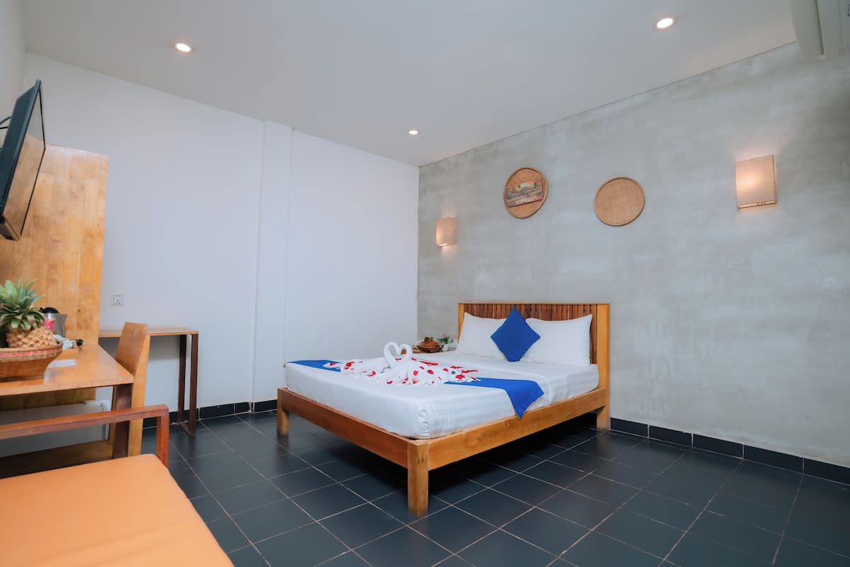 A modern hotel room with a wooden bed, a dining table with chairs, and a small kitchen area.