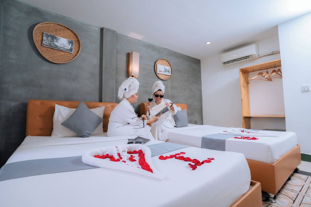A hotel room with two beds, a wooden headboard, a wall-mounted air conditioner, and a wooden wardrobe.