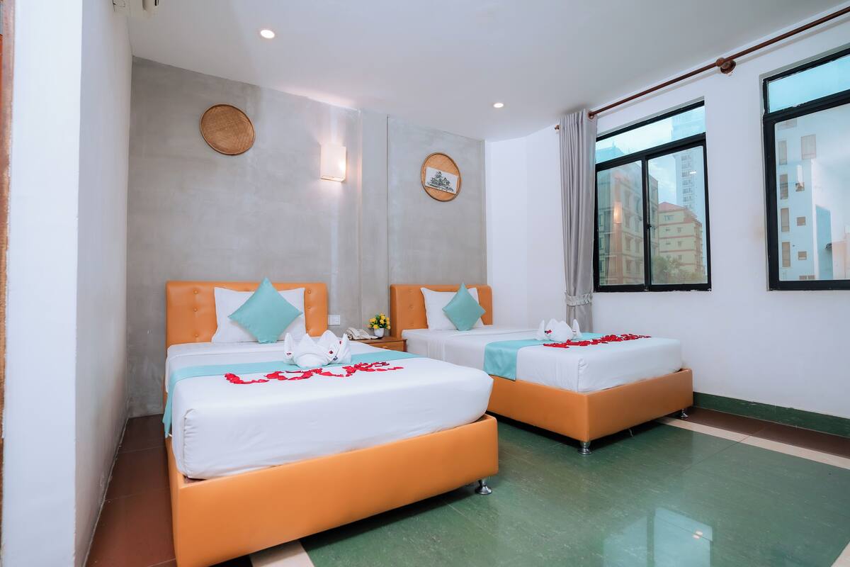 A hotel room with two beds, a large window, and a view of buildings.