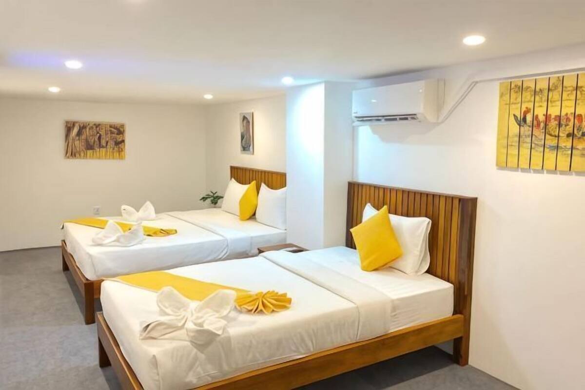 A hotel room with two beds, each with white bedding and yellow accents, wooden headboards, and artwork on the walls.