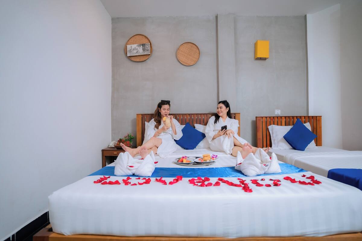 A hotel room with two beds, a wooden headboard, and a small table with a tray of food and drinks.