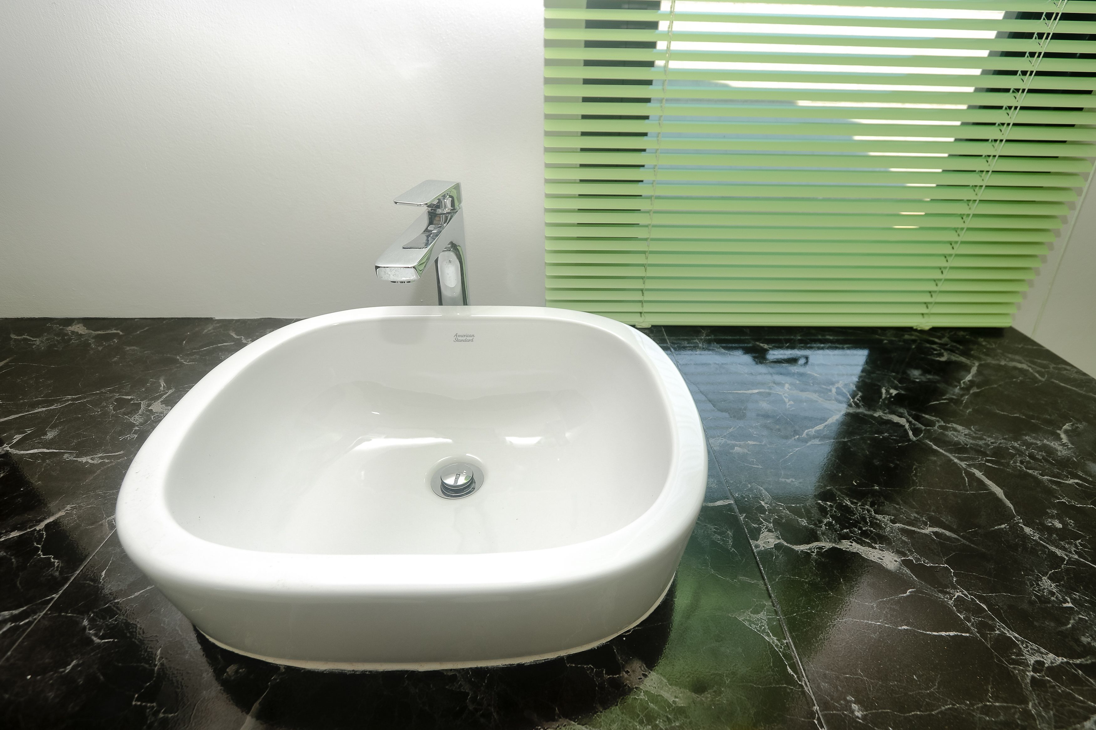 A bathroom with a white sink, black marble floor, and green blinds.
