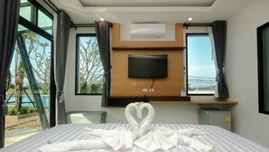 A hotel room with a bed, a TV mounted on the wall, and a view of the sea through large windows. - Saichon Grand View Resort (Ban Ta Khun)