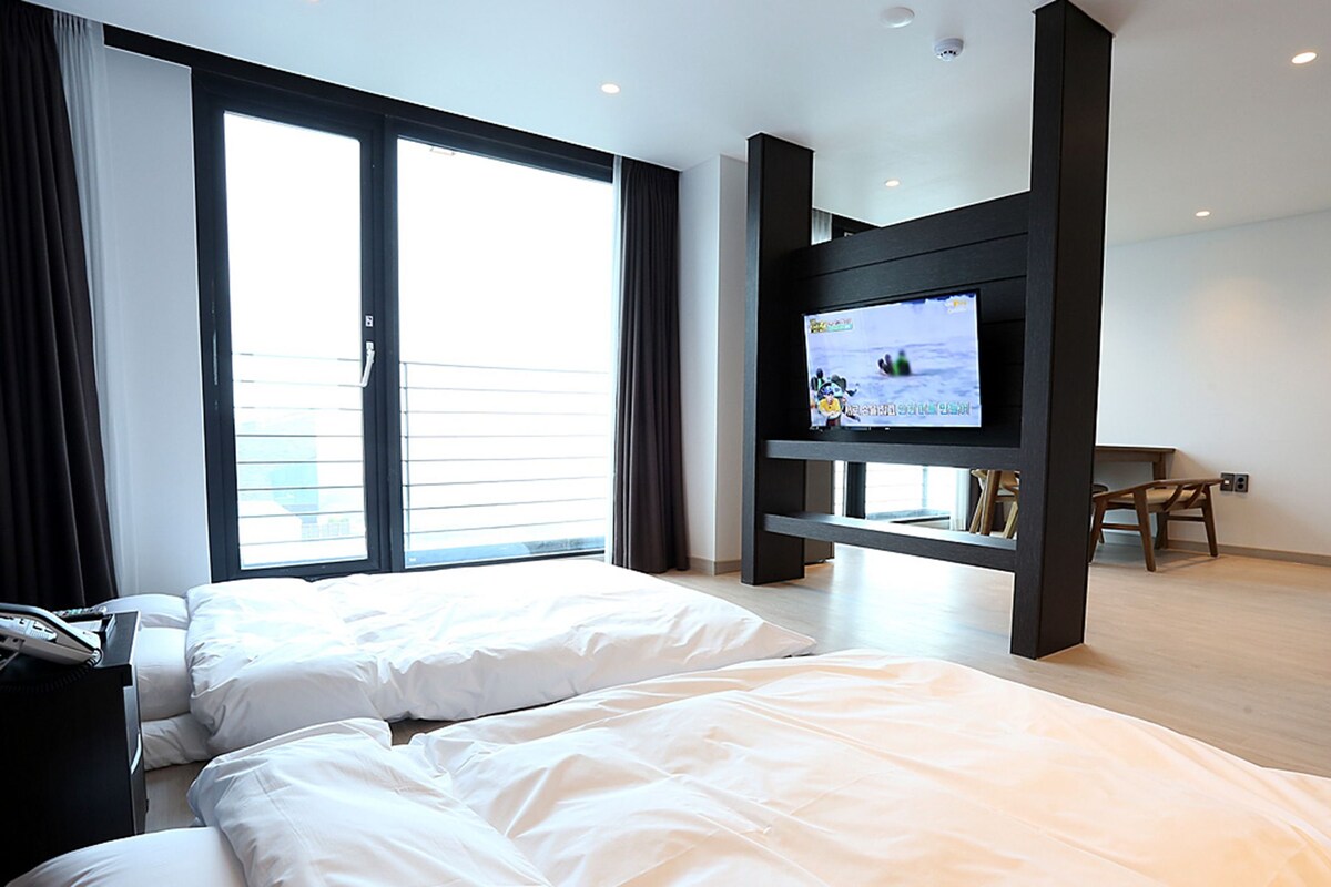 A hotel room with two beds, a TV, a desk, and a chair.