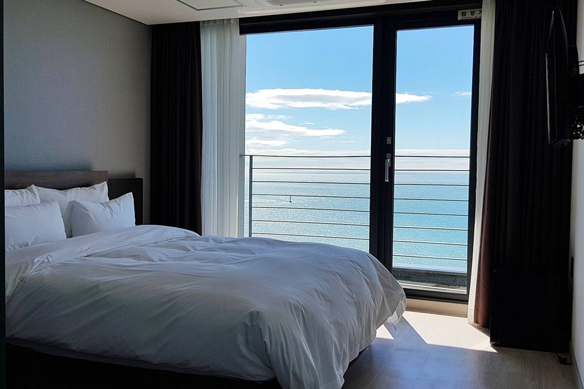Et hotelværelse med en stor seng, havudsigt gennem en skydedør og en balkon med gelænder.