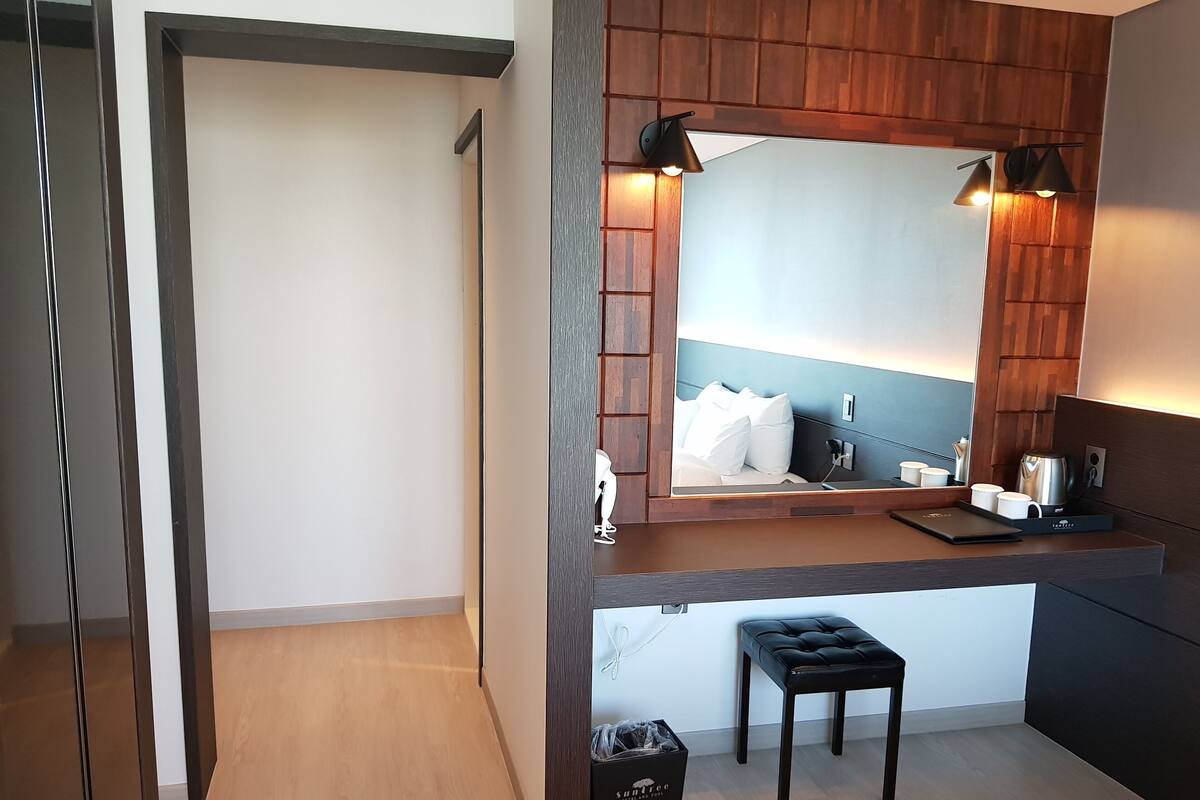 Et moderne hotelværelse med et træbord, et stort spejl, en lille skammel og en skraldespand.