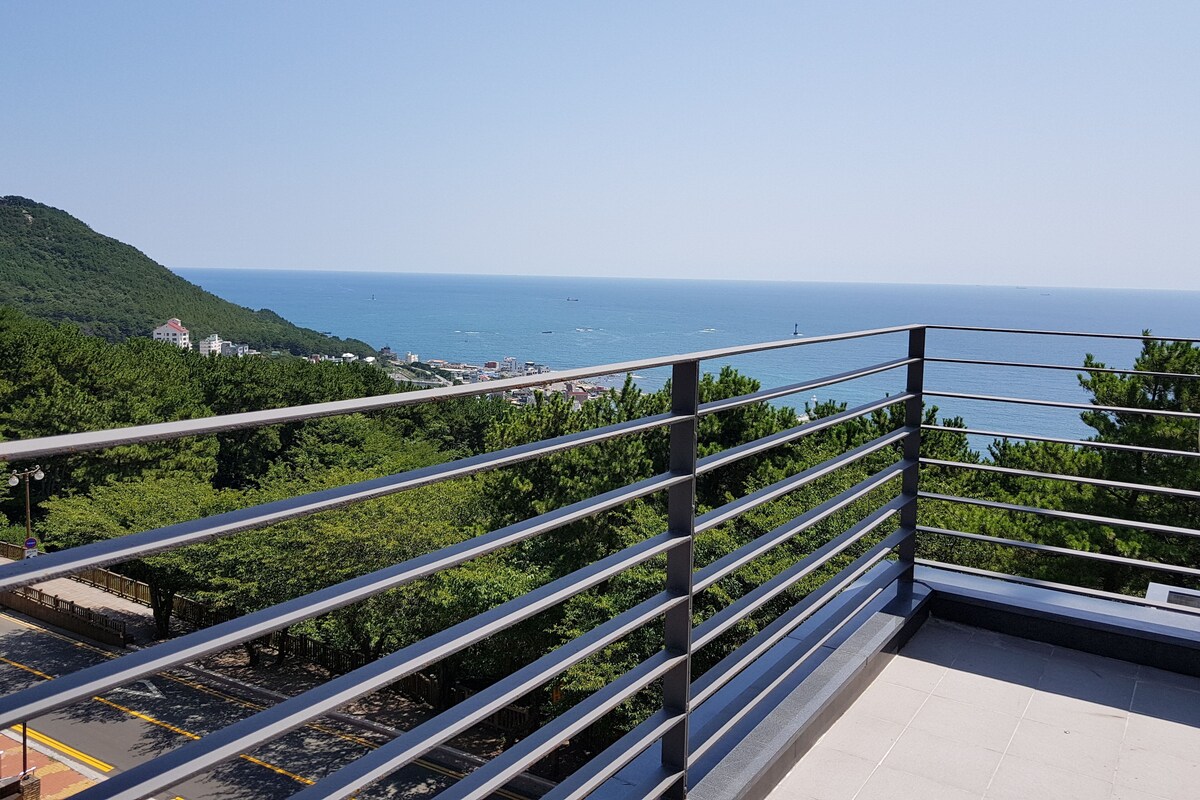 A balcony with a metal railing overlooking a coastal area with greenery and a view of the sea.