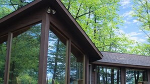 A cabin with large windows, a wooden deck, and a forest backdrop. - Pine Cottage on Blass Lake (Wisconsin Dells)