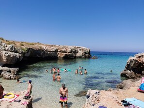 A rocky beach with clear water, people swimming, and a boat in the distance. - In the Villa by Aunt Tina (Bari)