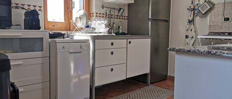 A compact kitchen with white cabinets, a built-in dishwasher, a stainless steel refrigerator, and a tiled backsplash.