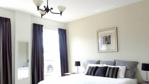 A hotel room with a large bed, a chandelier, a framed picture on the wall, and a window with curtains.