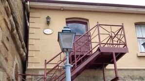 A building with a stone facade, a red metal staircase, and a blue street lamp.