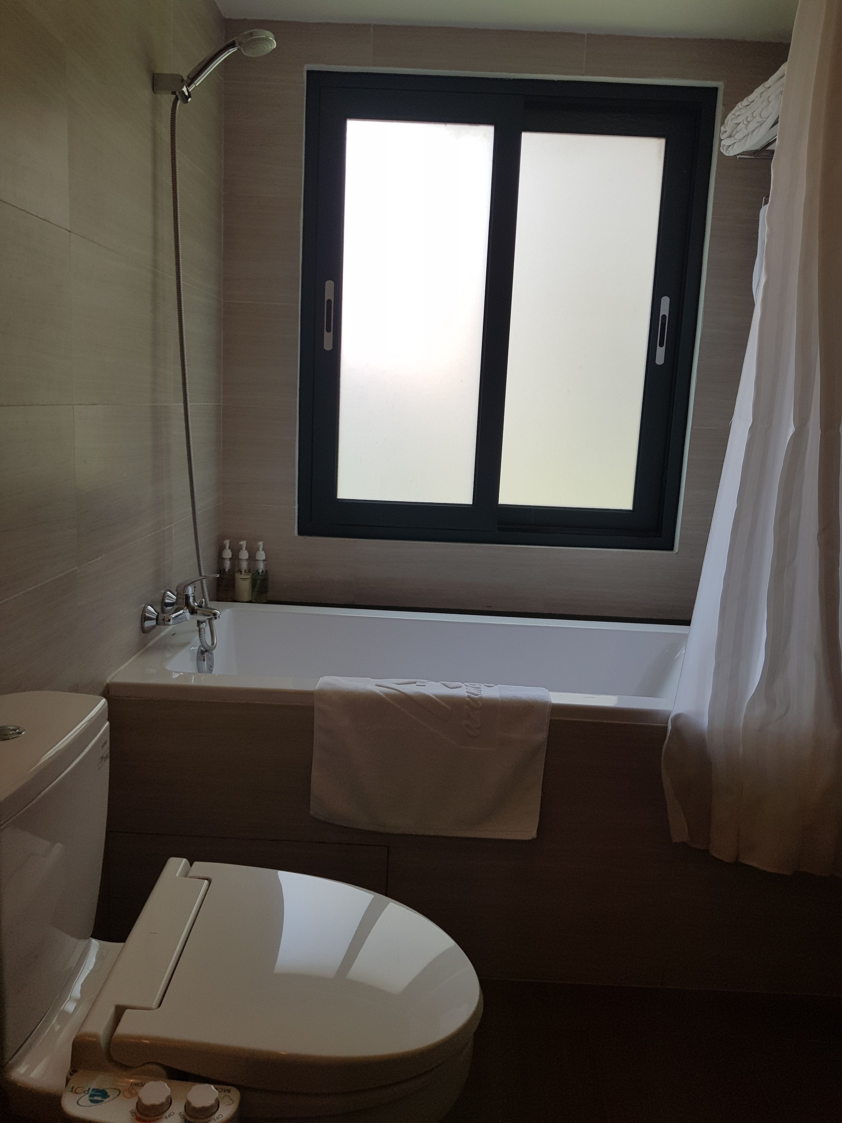 Une salle de bain avec une baignoire, des toilettes, une fenêtre et une douche.