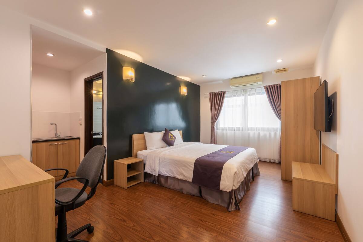 Une chambre d’hôtel moderne équipée d’un lit, d’un bureau, d’une chaise et d’un téléviseur fixé au mur.