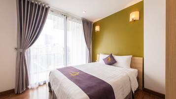A hotel room with a large bed, a headboard with a light fixture, and a window with curtains.