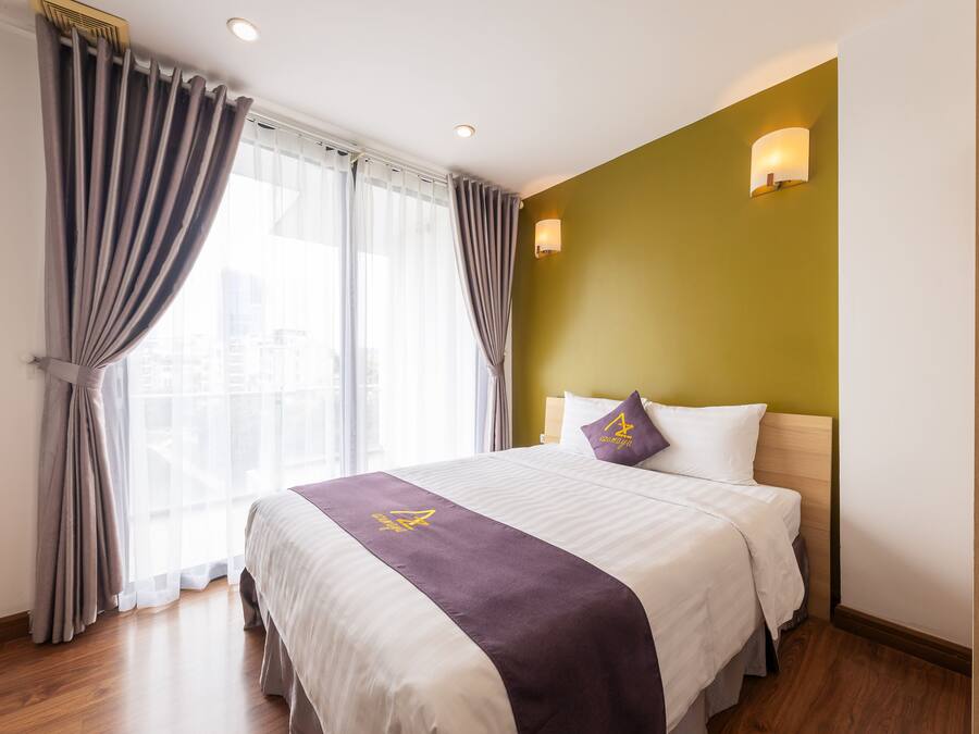 A hotel room with a large bed, a headboard with a light fixture, and a window with curtains.