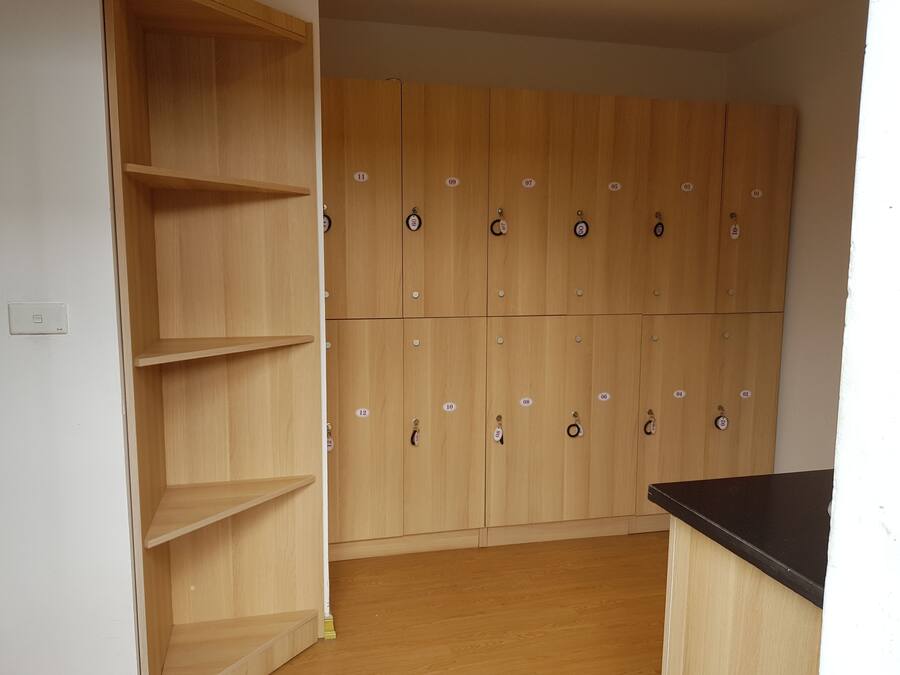A room with wooden lockers, a black countertop, and a white wall with a light switch.