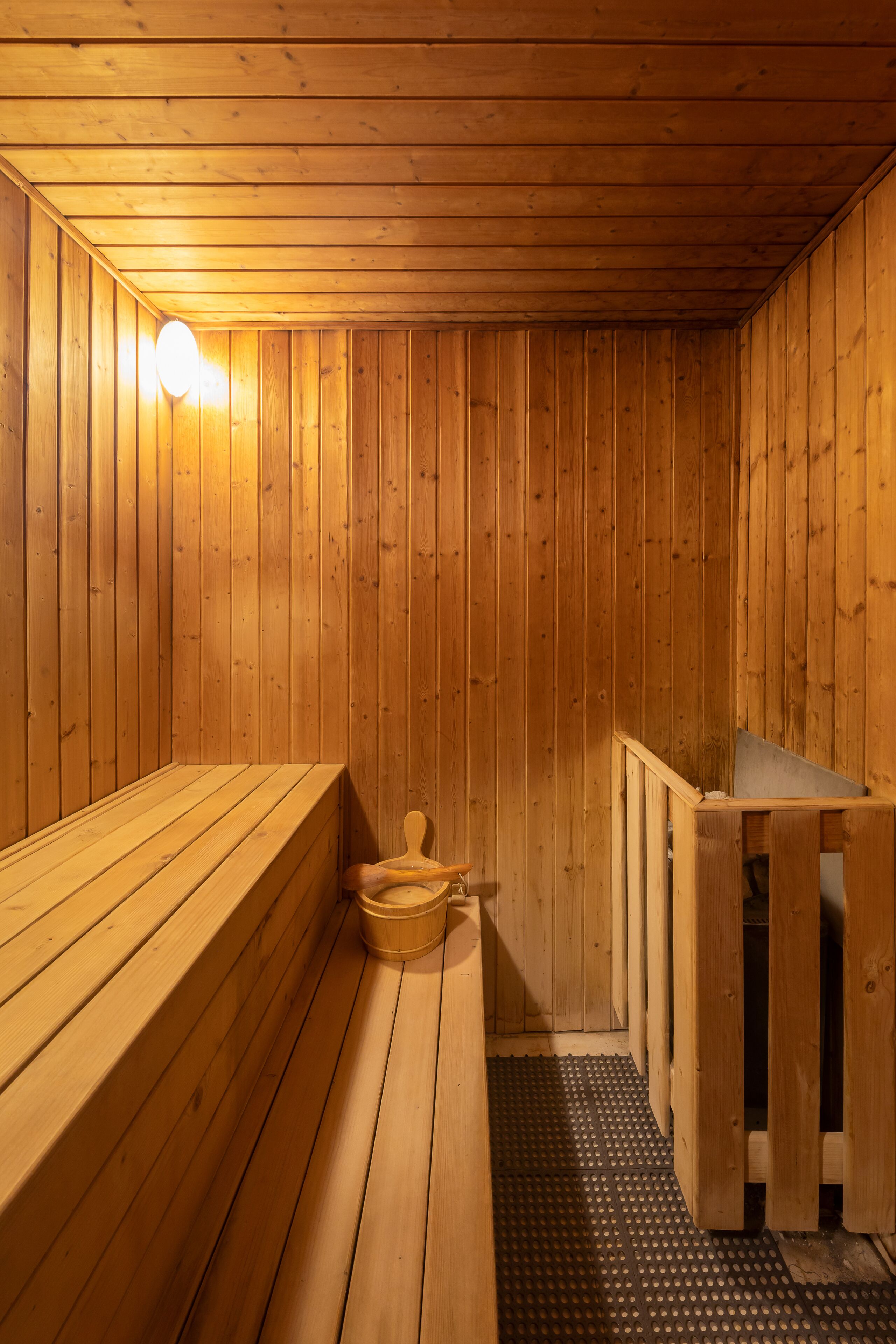 A wooden sauna with benches, a small wooden tub, and a wall-mounted light fixture.