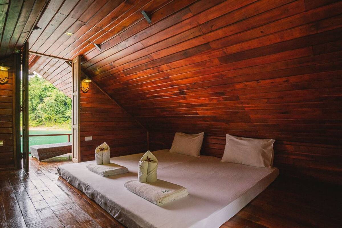 A cozy, wooden cabin bedroom with a large bed, pillows, and a bench by the window.