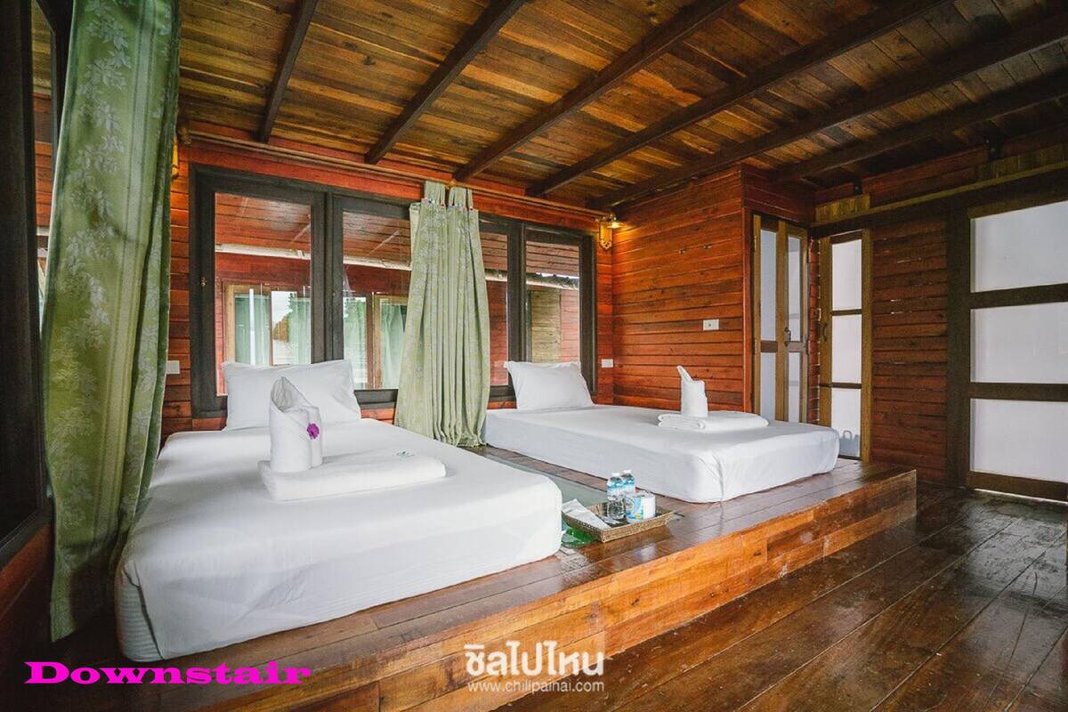 A wooden cabin with two beds, each with white linens and pillows, and a small table with a bottle and a cup.