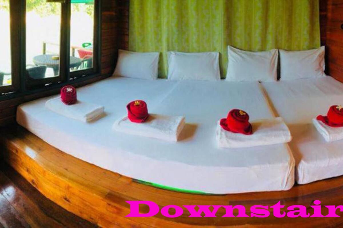 A large bed with white linens and red decorative pillows in a room with wooden flooring and green curtains.