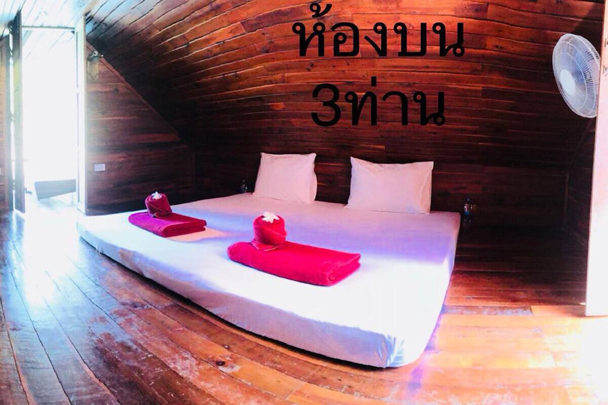 An upper room with wooden walls and a sloped ceiling, featuring two beds with red towels and white pillows.
