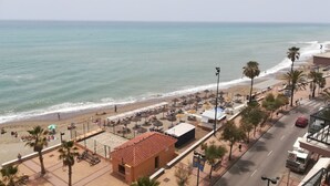 A beachside view with a road, beach umbrellas, and a small building. - Stunning views to the sea / Fuengirola Apartment (Fuengirola)