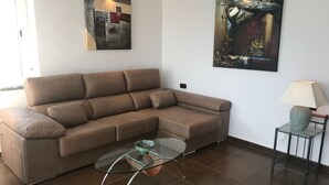 A living room with a brown sectional sofa, a glass coffee table, a small side table with a lamp, and two pieces of wall art. - Stunning views to the sea / Fuengirola Apartment (Fuengirola)