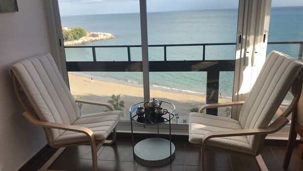 A balcony with two white cushioned chairs facing a beach view. - Stunning views to the sea / Fuengirola Apartment (Fuengirola)