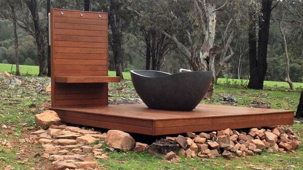 A modern outdoor seating area with a wooden bench and a large black bowl. - Idyllic Farm Cottage with Outdoor Bath Under the Stars (Manildra)