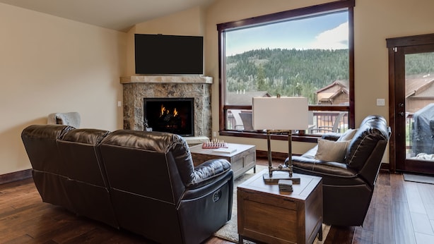 A living room with a fireplace, leather sofas, a coffee table, and a large window offering a view of a forested area. - Luxury Home, Private Hot Tub, Enjoy Keystone, Breckenridge, A Basin, Copper! (Keystone)