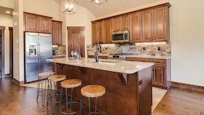 A spacious kitchen with wooden cabinets, a stainless steel refrigerator, a microwave, and a large island with stools. - Luxury Home, Private Hot Tub, Enjoy Keystone, Breckenridge, A Basin, Copper! (Keystone)