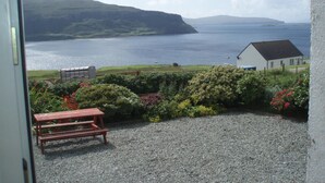 A view from a window overlooking a body of water, a grassy area, and a white building with a dark roof. - SPACIOUS FAMILY FRIENDLY - AMAZING SEA VIEWS - SLEEPS 4-6 (Isle of Skye)