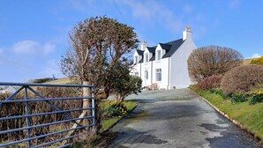 A rural road leading to a white house with a steep driveway, surrounded by trees and a metal gate. - SPACIOUS FAMILY FRIENDLY - AMAZING SEA VIEWS - SLEEPS 4-6 (Isle of Skye)