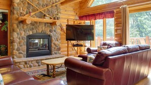 A cozy log cabin interior with a stone fireplace, leather sofa, and a flat-screen TV.