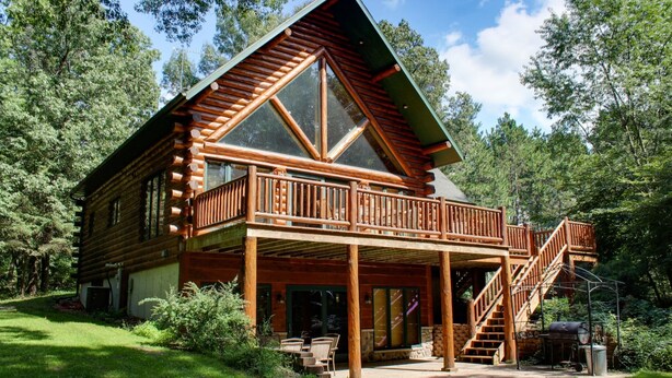 A log cabin with a balcony, a covered porch, and a staircase leading to the upper level.