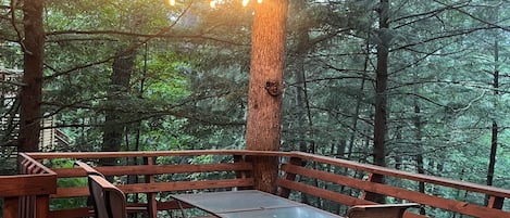 An outdoor wooden deck with a metal table and chairs, surrounded by trees and string lights.