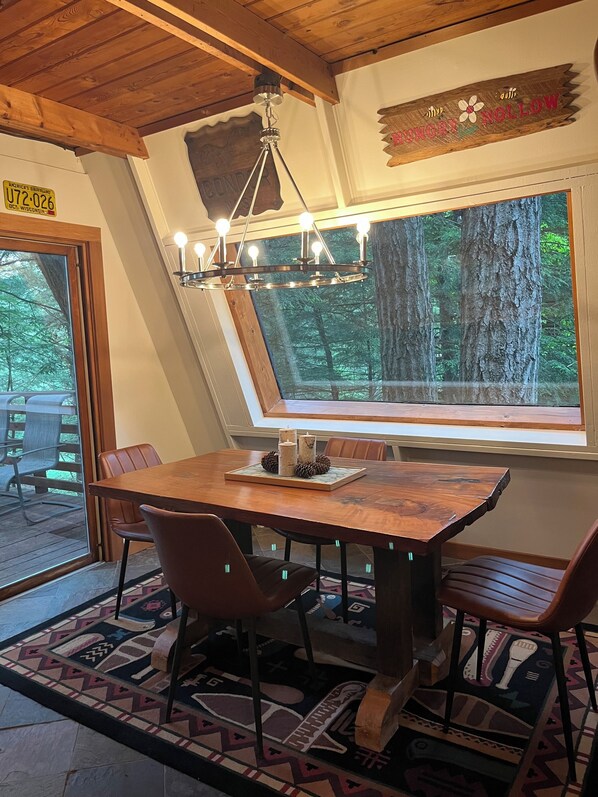 A dining area with a wooden table, chairs, a chandelier, and a large window with a forest view. - Nord Haus on Dell Creek Channel (Baraboo)