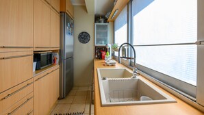 Une cuisine compacte avec des meubles en bois, un réfrigérateur en acier inoxydable, un four à micro-ondes et un évier placé sous une fenêtre.