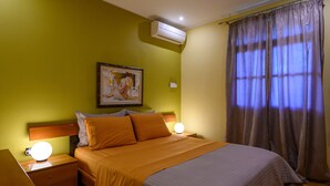 Une chambre d’hôtel comprenant un lit, deux tables de chevet avec des lampes, un climatiseur fixé au mur et une fenêtre avec des rideaux.