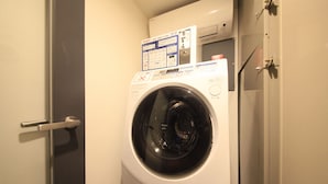 Un lave-linge à chargement frontal doté d’un panneau de commande, situé dans une pièce avec une porte et un climatiseur fixé au mur.